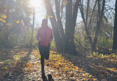Sonbahar sonbahar ormanlarında koşan bir kadın. Profilde kadın koşucu eğitimi. Dışarıda koşan genç Asyalı bir kadının sağlıklı yaşam tarzı görüntüsü. Etnik Kafkas fitness modeline uygun. Yüksek kalite fotoğraf