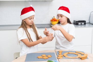 Çocuklar sıcak ev mutfağında Noel kurabiyeleri pişiriyorlar. Noel Baba şapkalı şirin çocuklar aile için tatil yemeği hazırlıyorlar. Kız kardeşler Xmas bisküvisi pişirir. Yaşam tarzı anı. Çocuk aşçı konsepti. Yüksek kalite fotoğraf