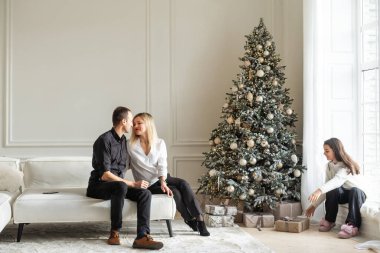 Mutlu Noeller ve mutlu tatiller. Anne, baba ve çocuk hediye değiş tokuşu. Ebeveynler ve kızları kapalı alanda eğleniyorlar. Odada hediyeleri olan sevgi dolu bir aile. Yüksek kalite fotoğraf