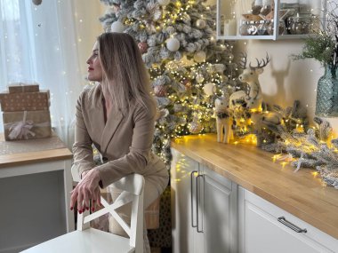 Sıcak bir tatil ortamında eğlenen bir kadın. Genç bir kadın, süslü bir Noel ağacıyla süslenmiş rahat bir oturma odasında dinleniyor. Yüksek kalite fotoğraf