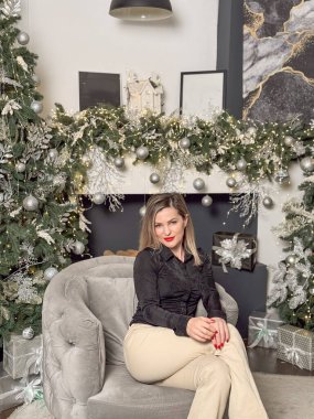 Sıcak bir tatil ortamında eğlenen bir kadın. Genç bir kadın, süslü bir Noel ağacıyla süslenmiş rahat bir oturma odasında dinleniyor. Yüksek kalite fotoğraf