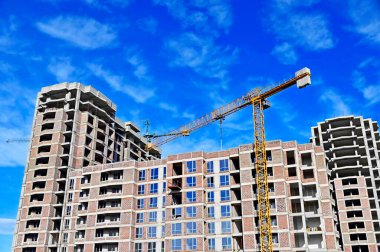 Vinçli ve mavi gökyüzü olan çok katlı bir inşaat alanı.