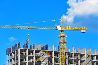 Vinçli ve mavi gökyüzü olan çok katlı bir inşaat alanı.