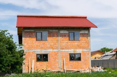Pencereleri ve çatısı olan tamamlanmamış bir tuğla ev, inşaat ve kentsel gelişimi vurguluyor