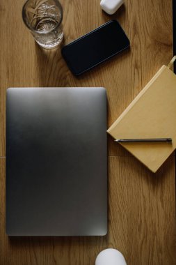Conceptual vertical top view photo of a laptop, notebook, phone and a glass of water on a wooden table.