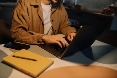 Bearded man typing on laptop at night in kitchen close-up