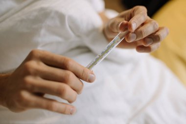 A man holds a thermometer in his hands to measure body temperature in bed. conceptual photo