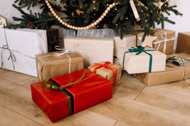Güzel dekore edilmiş bir Noel ağacının altında paketlenmiş hediyeler. Sıcak ışıkları ve doğal ahşap zemini olan rahat bir tatil evi.