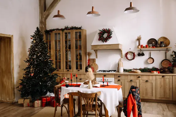 Noel için ağaç, şenlik masası ve doğal bayram dekoruyla dekore edilmiş sıcak bir köy mutfağı. Yumuşak gün ışığıyla sıcak aile ortamı.