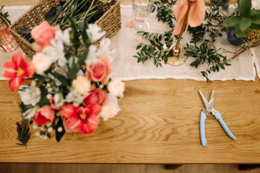 Çiçekler, makas ve buket yapmak için doğal malzemeler içeren kırsal bir masa.