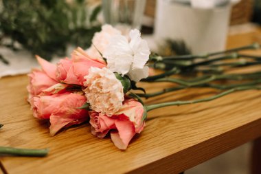 Pembe güller ve pembe karanfiller bir buket oluşturmadan önce masanın üzerinde uzanıyorlar.