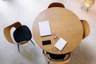 Yuvarlak ahşap masa, kapalı dizüstü bilgisayar, not defteri ve bir fincan kahve. Minimalist çalışma alanı ya da ev ofisi.