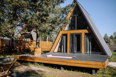 Doğadaki modern A çerçeveli ev. Terasa yayılmış yoga minderi olan ağaçlarla çevrili rahat, üçgen ahşap bir ev.