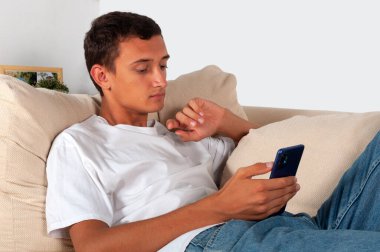 Cep telefonlu genç adam evdeki kanepede uzanıyor.