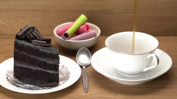 将热的黑咖啡倒入白色瓷杯 用白色陶瓷盘中的美味巧克力蛋糕和木制桌子上的小杯中的五颜六色脆饼倒入其中 — 图库视频影像