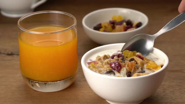 高角形的景色 一勺美味的松软麦片早餐 配以干枯的热带甜水果和新鲜牛奶 放在木制桌子上 配上一杯橙汁 — 图库视频影像
