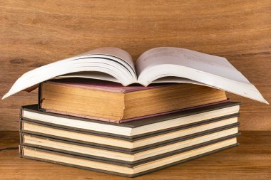 Ahşap masa üzerinde açık beyaz sayfalar olan koyu renkli ciltli kitap yığını..