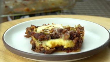 Springling parmesan cheese on a slice of delicious homemade italian food lasagna in rotation brown ceramic plate on wooden board.