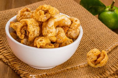 Yüksek açılı ev yapımı, bol yağda kızartılmış domuz derisi, beyaz seramik kâse, çuval bezi ve ahşap masa yapraklı yeşil limon..