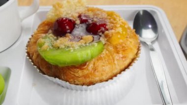 Beyaz plastik bir tepsi kahve molası. Lezzetli ev yapımı, karışık meyveli, bir parça kivi, bir parça ananas, kırmızı kiraz, yeşil üzüm ve bir fincan sade kahve ile süslenmiş..