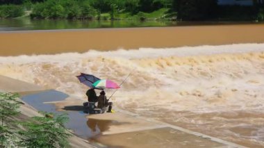İki balıkçı renkli şemsiyelerin altında Rapid River 'da balık tutuyor. Şiddetli yağmurdan sonra baraj taşar..