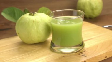 Taze guava suyuna şeffaf bardakla zum yapmak ahşap tahtada taze guava meyvesi ve ahşap masa üzerinde yeşil guava yaprakları..