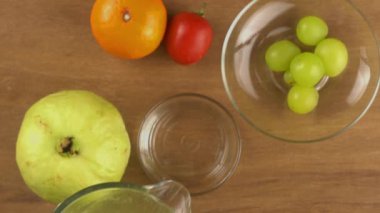 Yeşil guava suyunu şeffaf bardağa döküyor. İçinde guava meyvesi, portakal meyvesi, kırmızı domates ve şeffaf cam tabakta üzümler var..