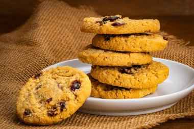 Yulaf ezmesi yığını ve yaban mersini bisküvisi beyaz seramik tabakta tahta masa üzerinde çuval bezi.