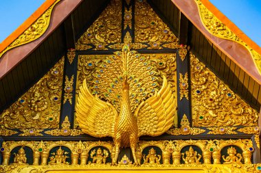 Sculpture of golden Peacock at the facade of main hall in a buddhist temple, Wat Phra That Doi Phra Chan in Lampang Province, Thailand. clipart