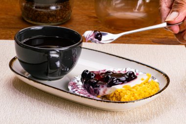 Beyaz seramik tepside yaban mersinli turtadan bir ısırık alıyorum siyah seramik kahve bardağıyla ahşap masada.