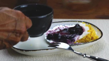 Yaşlı bir adam beyaz seramik tepside yabanmersinli peynirli turta ile sade kahve içiyor..