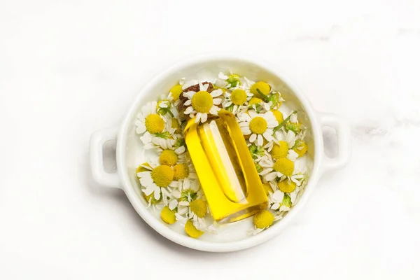 Daisy flowers and a bottle of olive oil in a white plate on a marble kitchen countertop in a top view