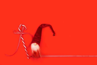 Kırmızı ve beyaz baston şekerler ve kırmızı arka planda fotokopi alanı olan Noel Baba bebeği