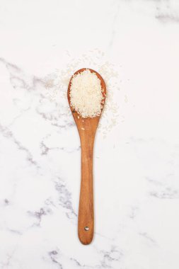 Tahta bir kaşıkta çiğ pirinç ve üst manzaralı mermer bir mutfak tezgahında