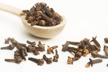 A heap of cloves in a wooden spoon and on a white background with copy space
