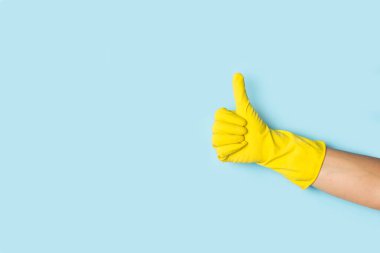 Woman hand with yellow rubber glove doing thumb up gesture on a light blue background with copy space