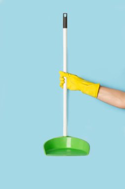 Woman with yellow rubber gloves holding a dustpan on a light blue background with copy space