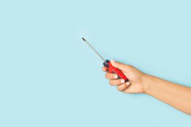 Woman hand holding a screwdriver on a light blue background with copy space