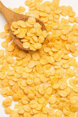 Corn flakes on a wooden spoon and on a white background in a top view