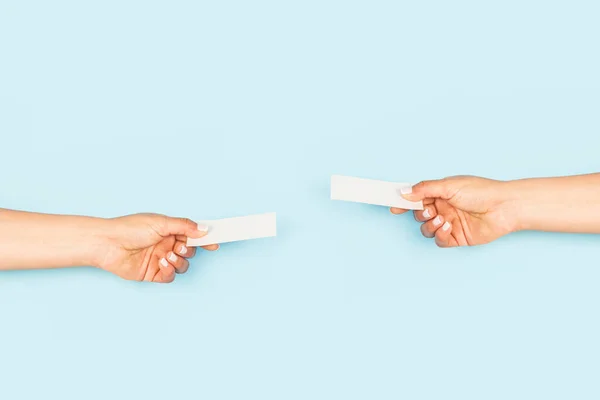 Women hands exchanging blank white personal cards on a light blue backgroud with copy space