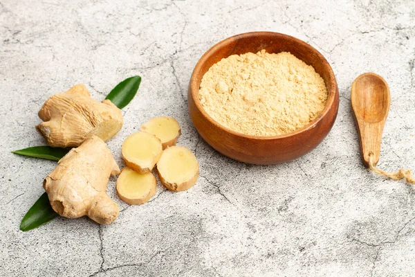 stock image Ginger powder in a wooden bowl and a ginger root on a stone background with copy space