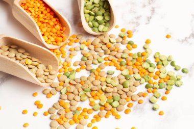 Ahşap kaşıklarda kırmızı, yeşil ve kahverengi mercimek ve beyaz mermer mutfak tezgahında fotokopi alanı var.