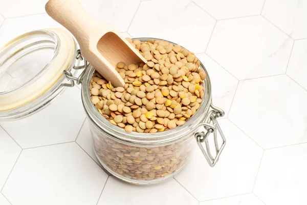 キッチンカウンターにコピースペース付きの木製スプーン付きのクリスタル瓶の中の茶色のレンズ豆 — ストック写真
