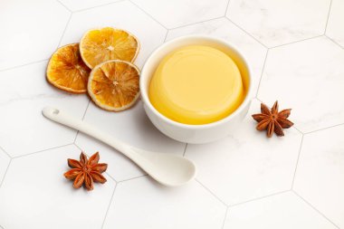 Beyaz kâse içinde ev yapımı vanilyalı puding. Kurumuş portakal dilimleri ve beyaz altıgen mutfak tezgahında yıldız anason.