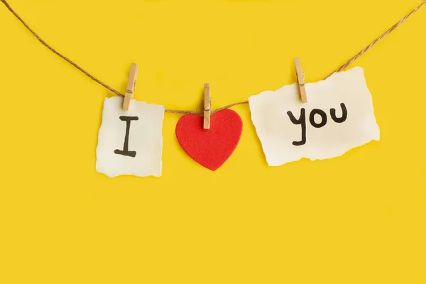 I love You phrase Made with text and a red hearts hanging from a thread on a yellow background