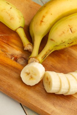 Muz ve dilimlenmiş muz ahşap mutfak tahtasının üstünde.