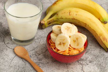 Bir avuç muz, bir bardak süt ve mermer mutfak tezgahındaki bir kasede kahvaltı gevreği.