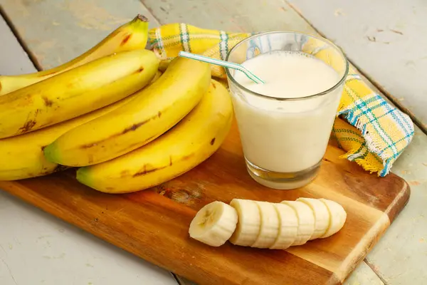Hand of bananas, a sliced banana and a glass of milk on a wooden kitchen board
