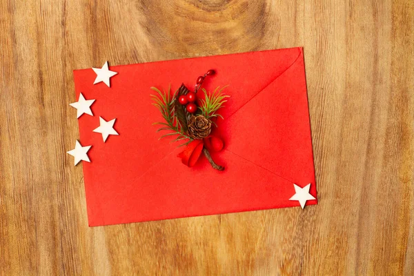 A red envelope with fir branch, hollies and white stars on a wooden background in a top view
