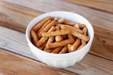 Tahta bir masada beyaz bir kasede küçük ekmek çubukları.